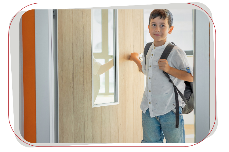 A young student wearing a backpack stands in a doorway, smiling at the camera.